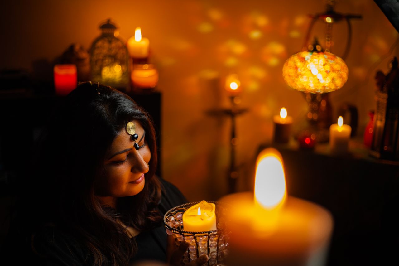 services-02 A woman embraces a tranquil moment surrounded by candlelight and warm glow in a cozy setting.
