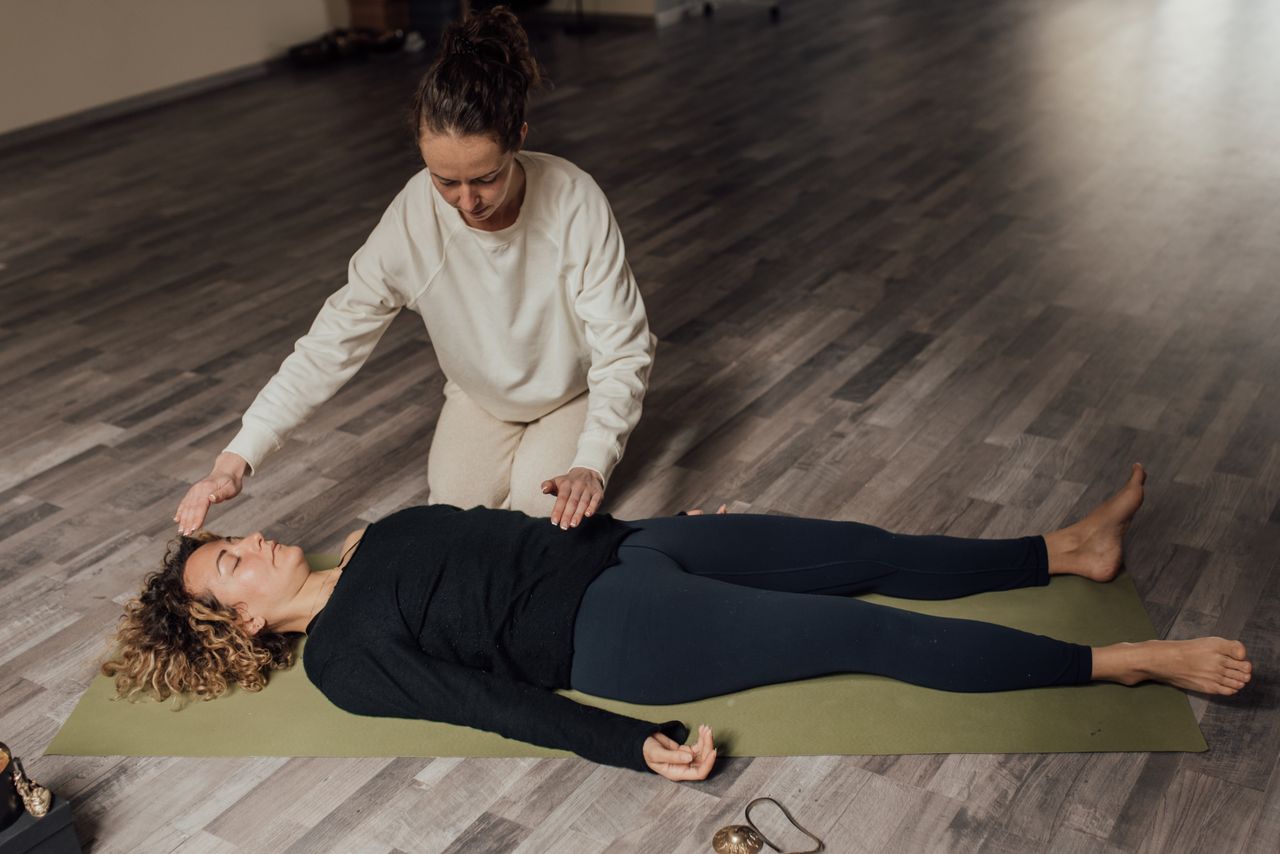 who-we-are Energy therapist healing barefoot female with closed eyes during meditation practice on floor in sunlight
